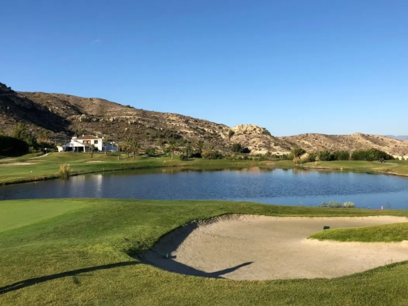 Scenic view of Font del Llop Golf Course in Spain, featuring lush green fairways, sand bunkers, water hazards, and surrounding mountainous terrain under a clear sky