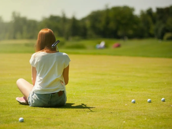 Young woman sitting on the Alicante Golf course with a putter, surrounded by golf balls on a sunny day.