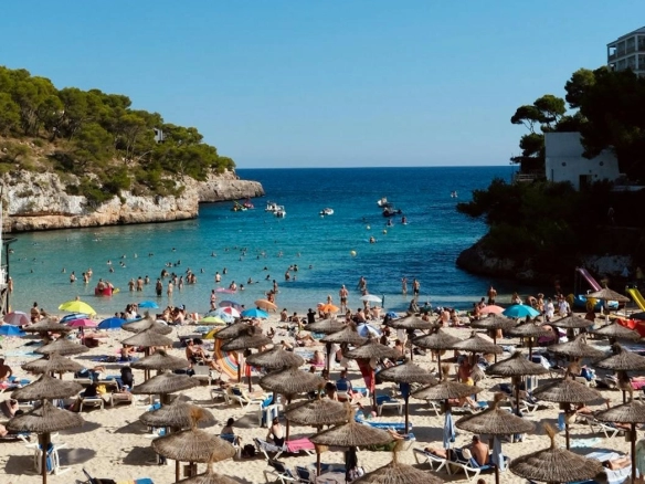 A crowded beach in Spain with turquoise waters, surrounded by cliffs and lush greenery, perfect for relaxation and golf enthusiasts exploring Golf Spain.