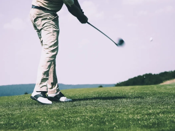Golfer mid-swing on lush green fairway at Roda Golf course in Murcia, Spain. Lower body and golf club visible against scenic backdrop of rolling hills.