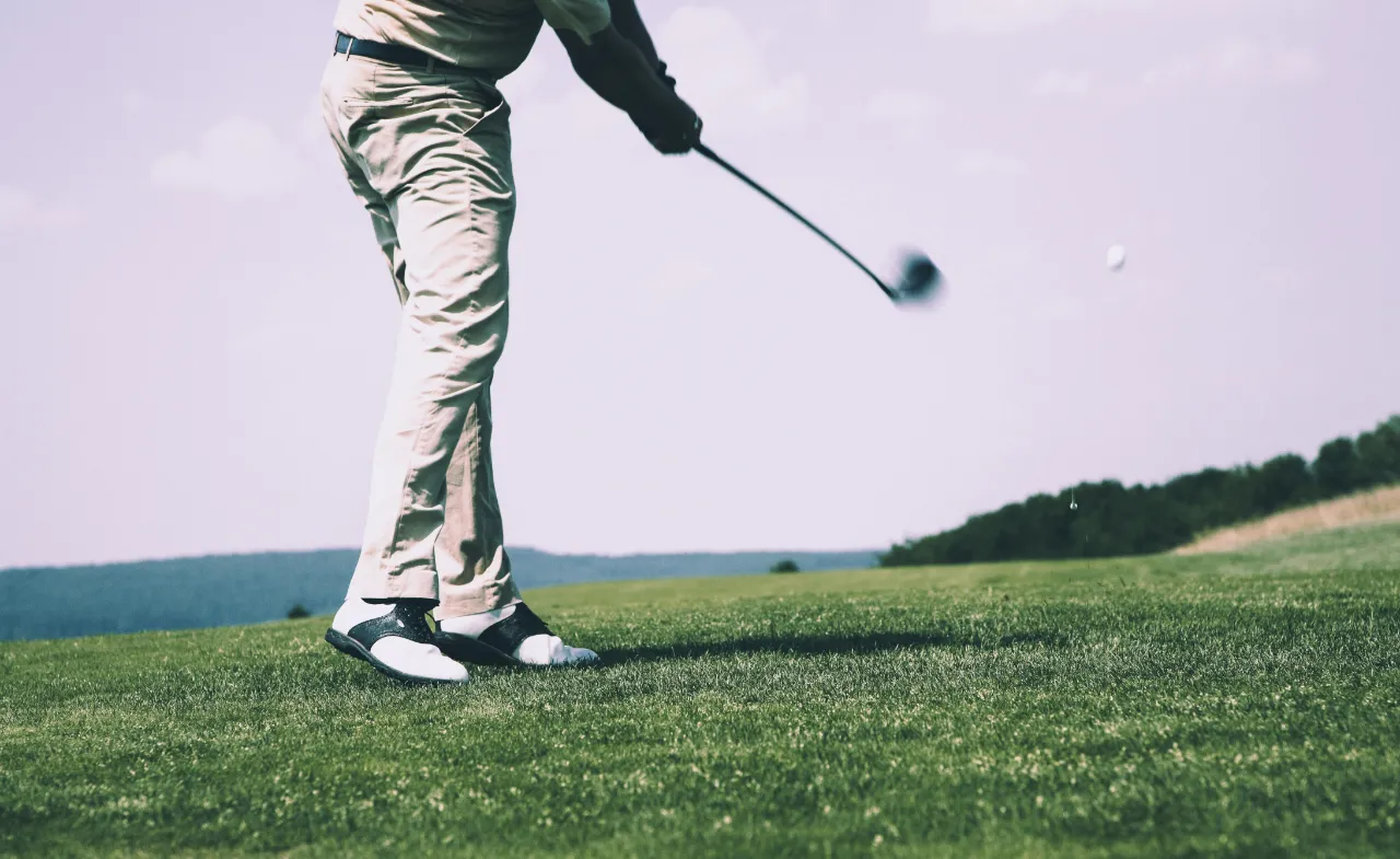 Golfer mid-swing on lush green fairway at Roda Golf course in Murcia, Spain. Lower body and golf club visible against scenic backdrop of rolling hills.