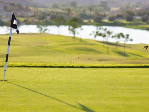 Scenic golf course in Murcia, Spain, with lush green fairway, flag on putting green, rolling hills, and water hazard in background