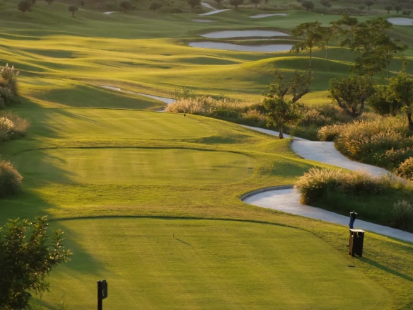 Scenic golf course in Moraira, Spain with lush fairways, winding cart paths, and water hazards under golden evening light