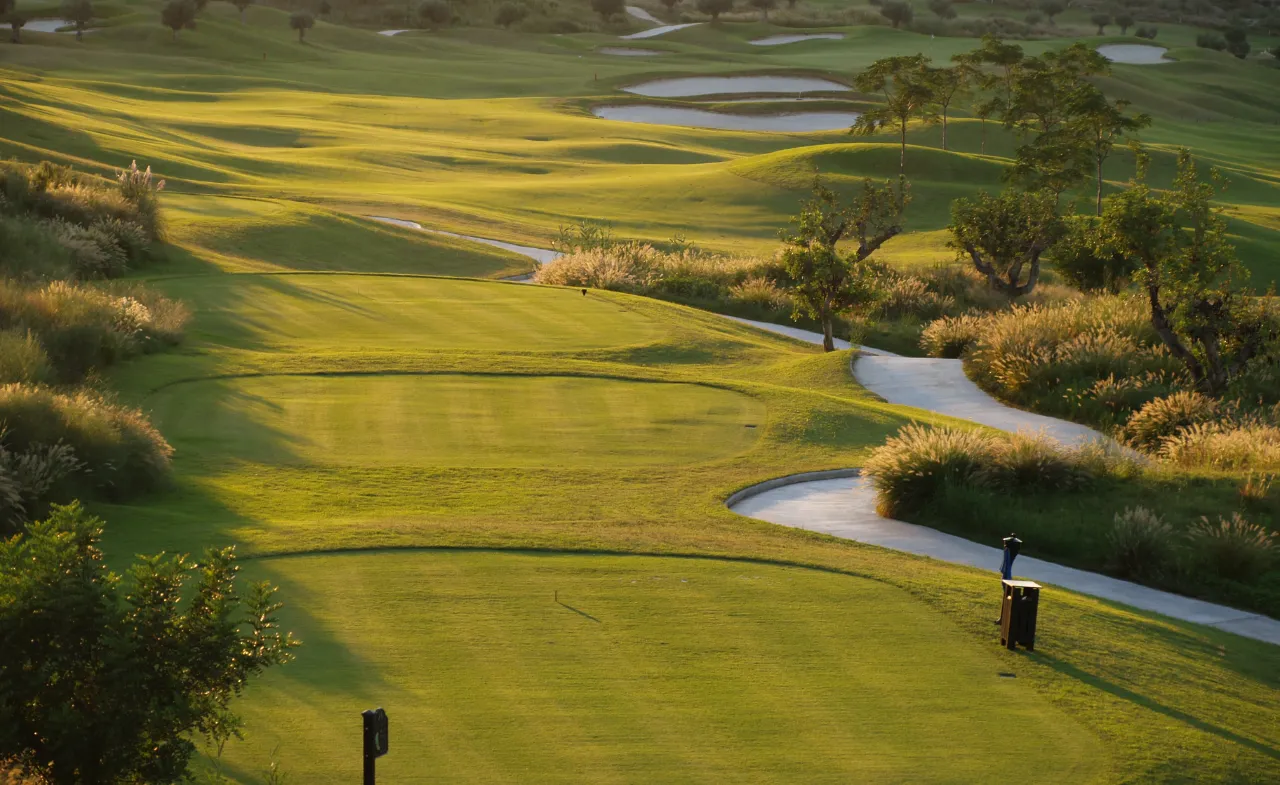 Scenic golf course in Moraira, Spain with lush fairways, winding cart paths, and water hazards under golden evening light